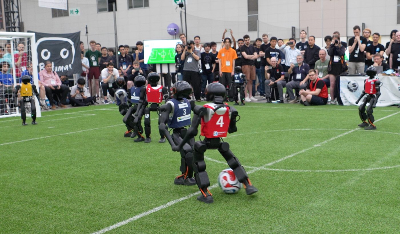 Booster K1 robots playing football in front of a crowd at RoboCup